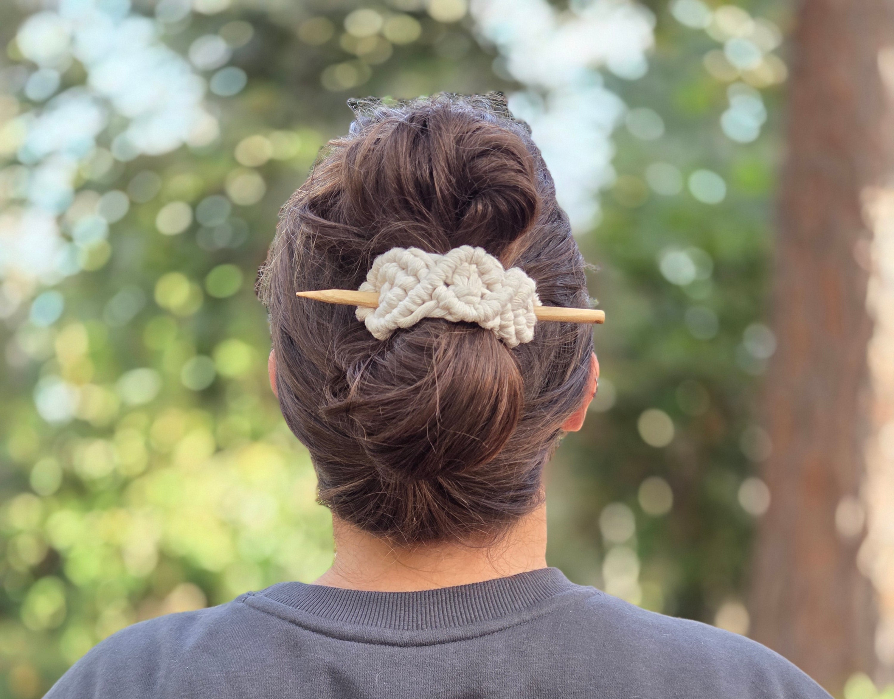 Person wearing a bun stick hair accessory in sweatshirt with a butterfly design and 'Let Life Fly' text, standing outdoors