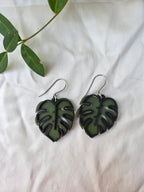 Green leaf-shaped earrings on a white fabric background