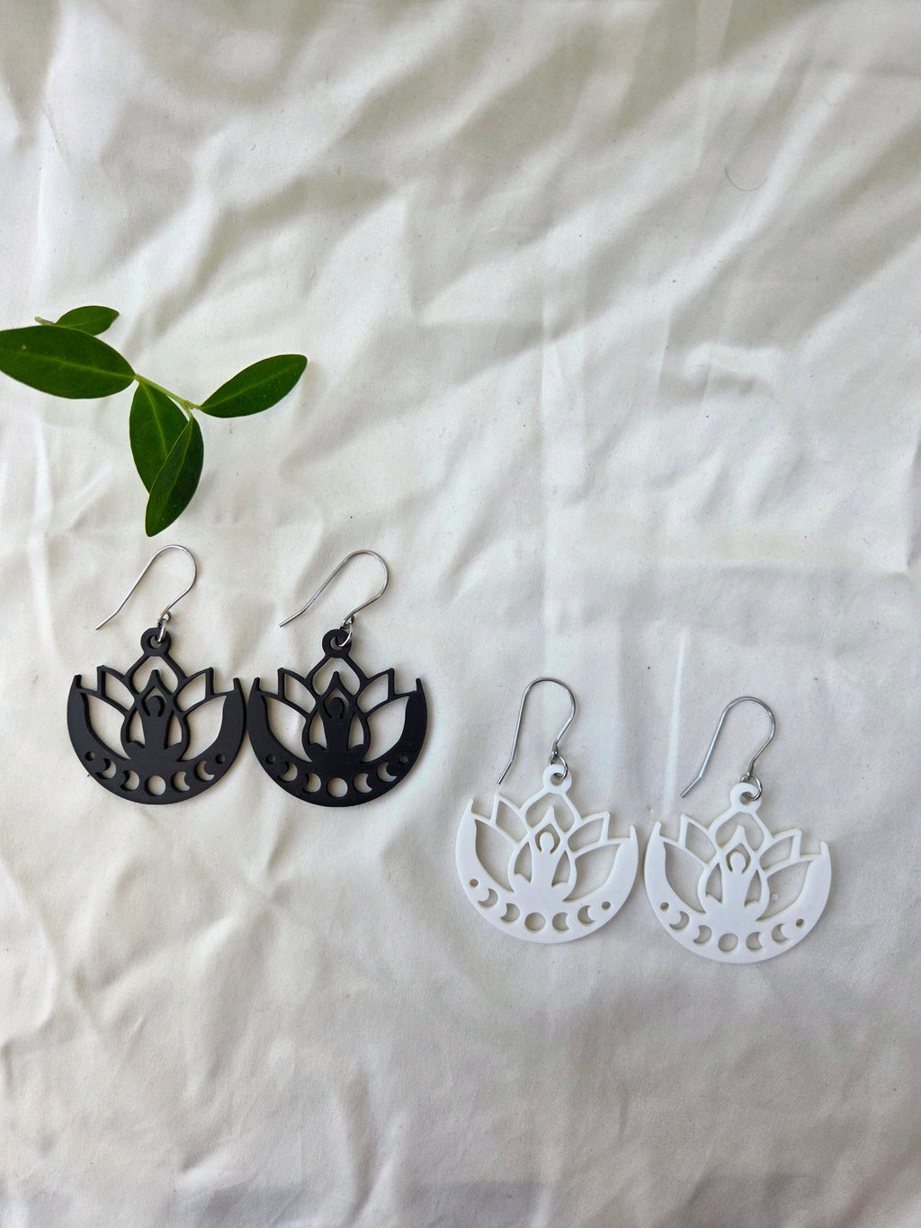 Black and white lotus flower earrings on a white fabric background with green leaves.