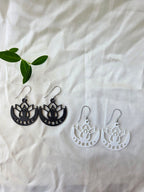 Black and white lotus flower earrings on a white fabric background with green leaves.