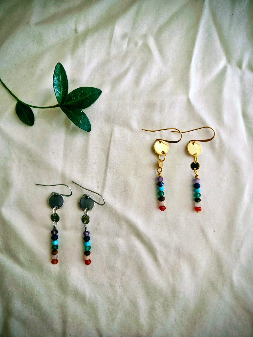 Pair of beaded earrings on a white fabric background with a green leaf.