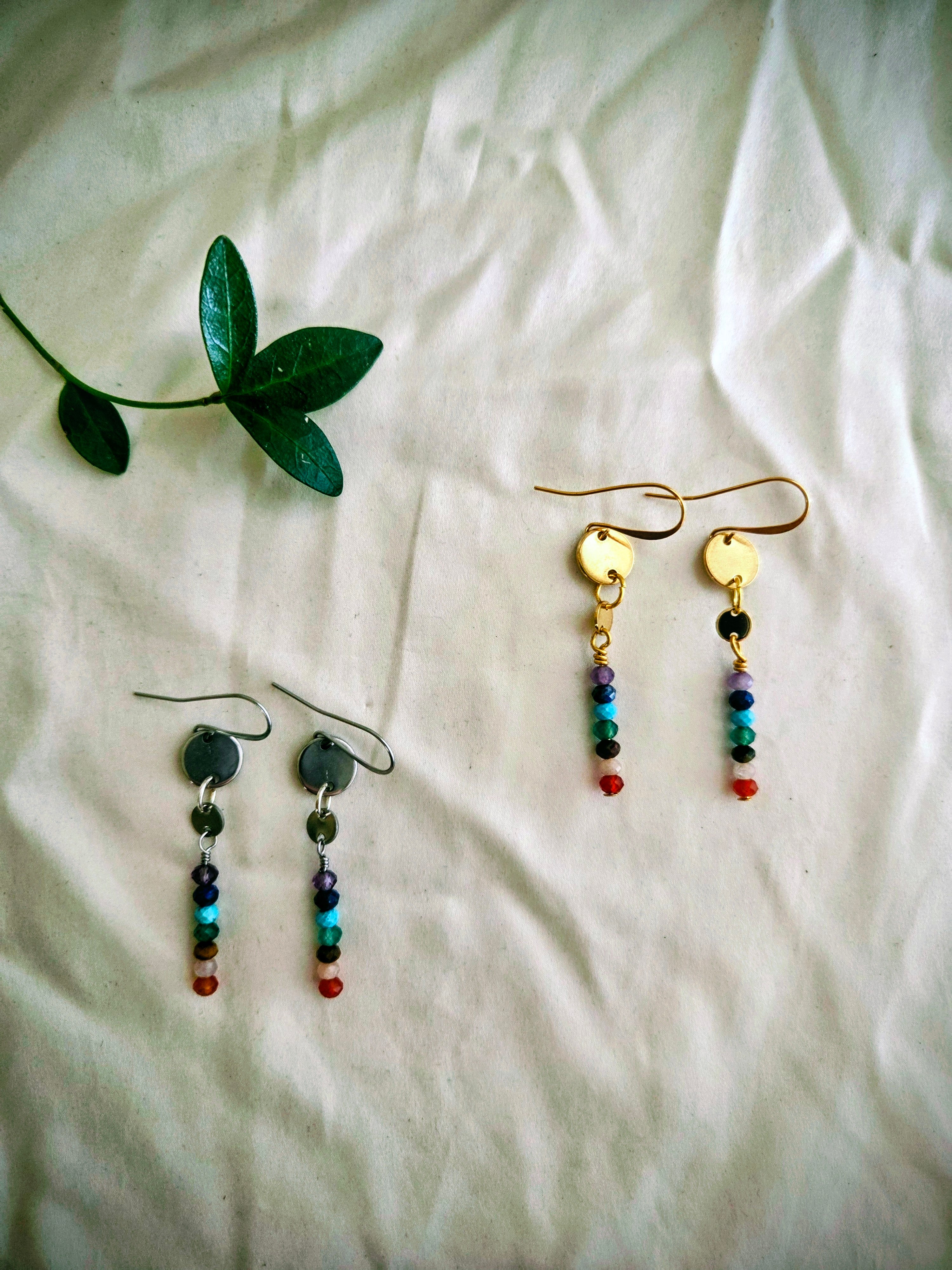 Pair of beaded earrings on a white fabric background with a green leaf.