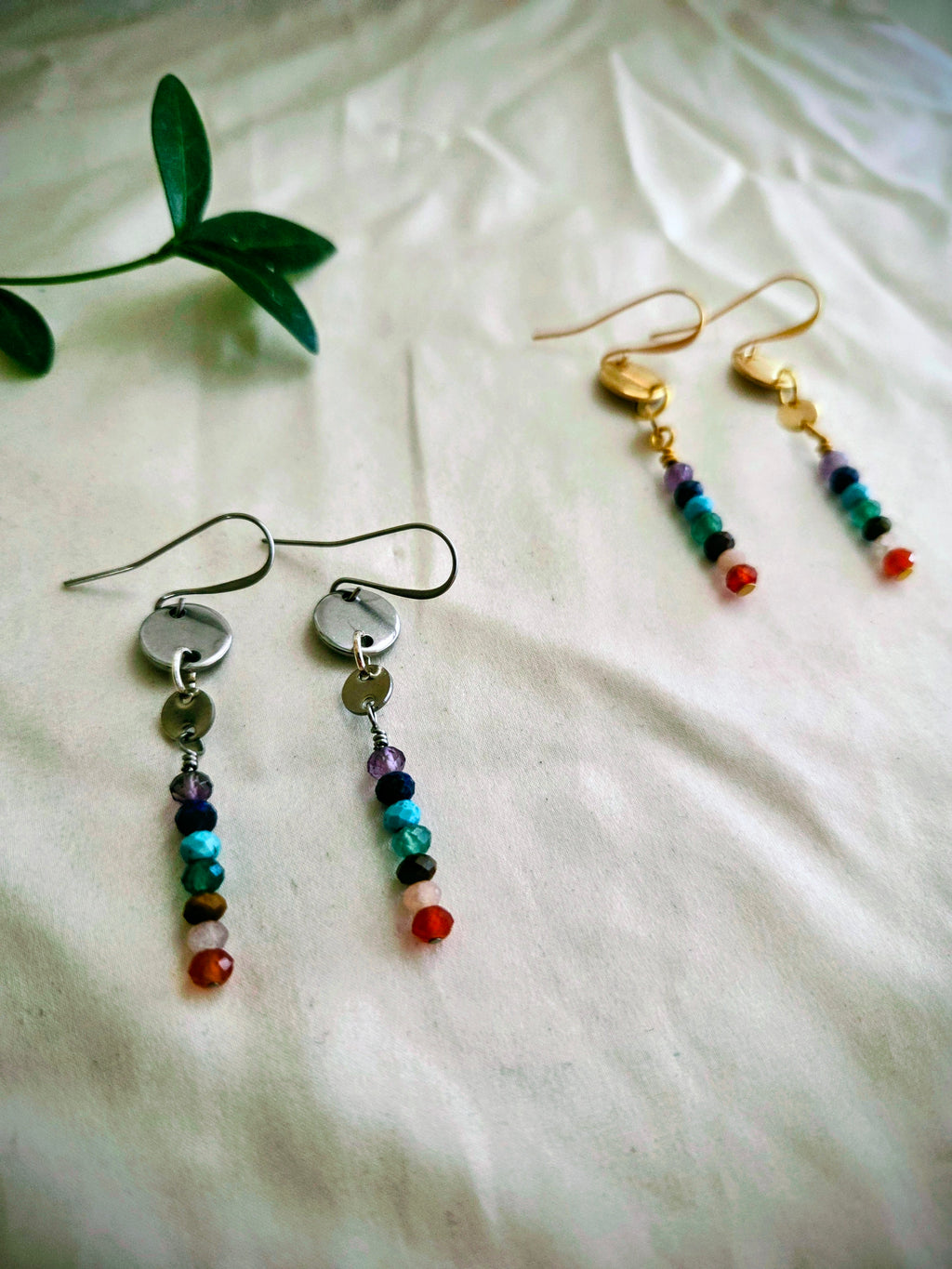 Colorful beaded earrings on a white fabric background with a green leaf.