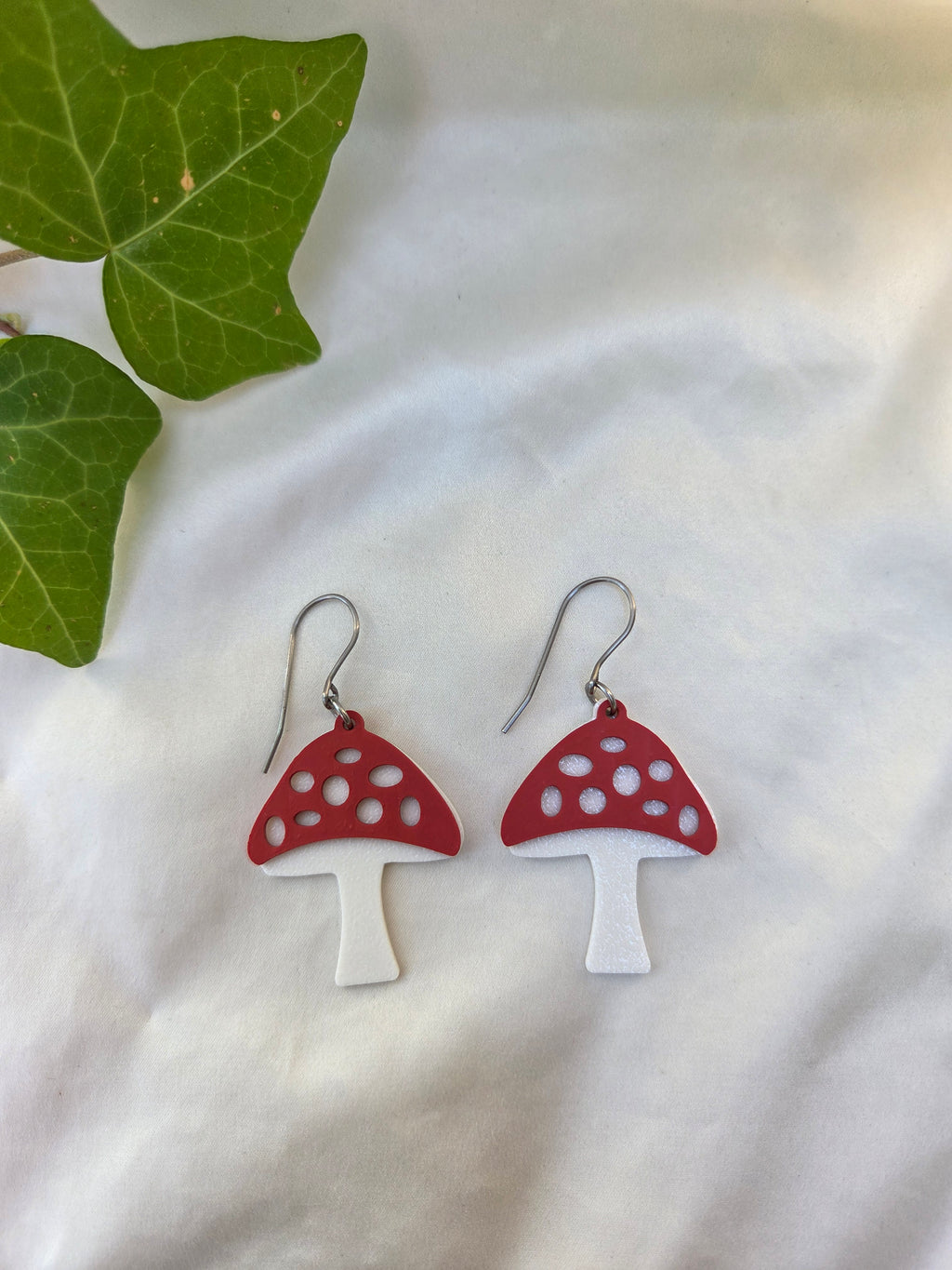 Mushroom-shaped earrings on a white fabric background with green leaves.