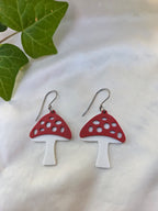 Red and white mushroom-shaped earrings on a light background with green leaves.