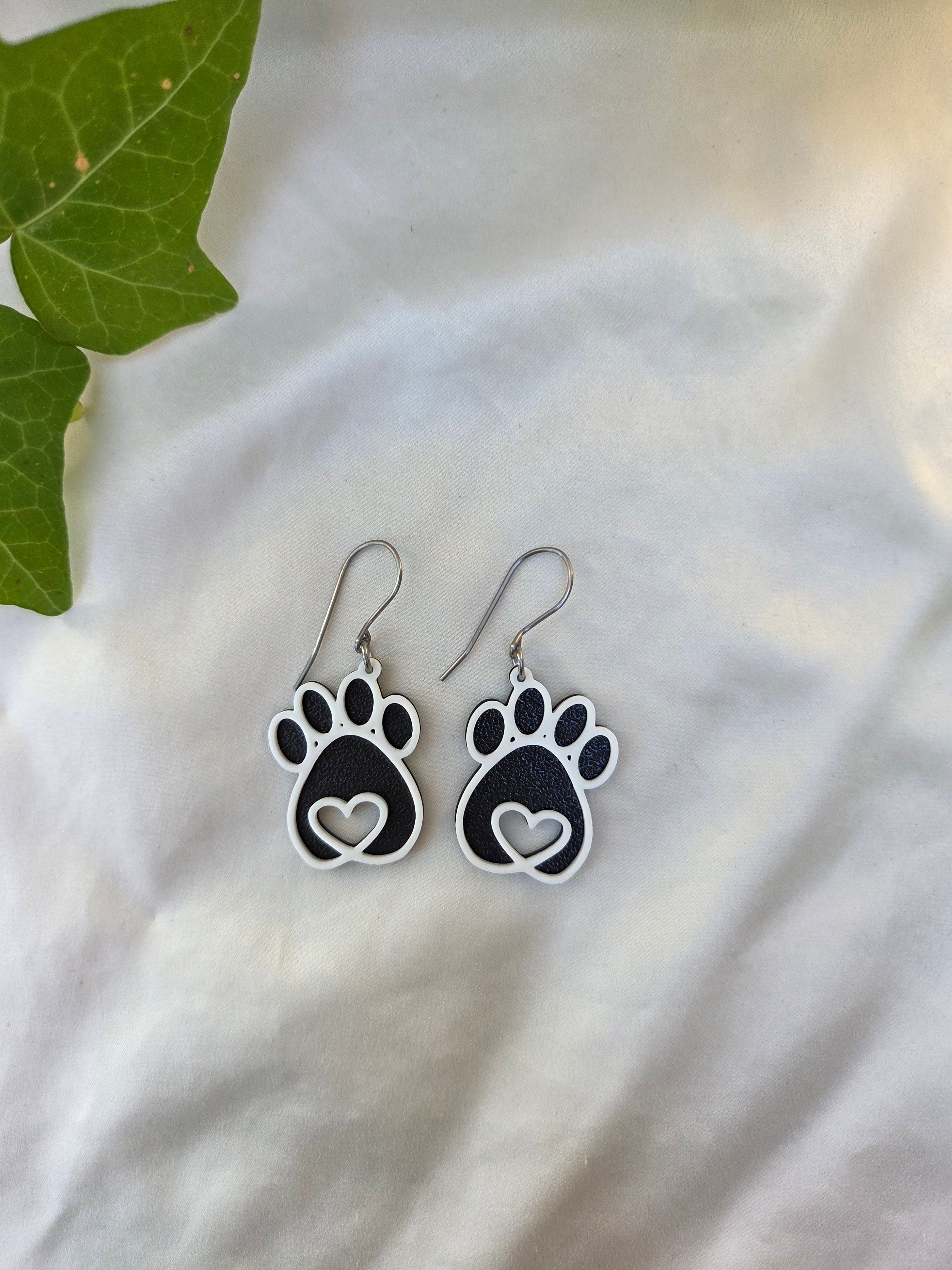Paw print earrings on a light fabric background with a leaf.