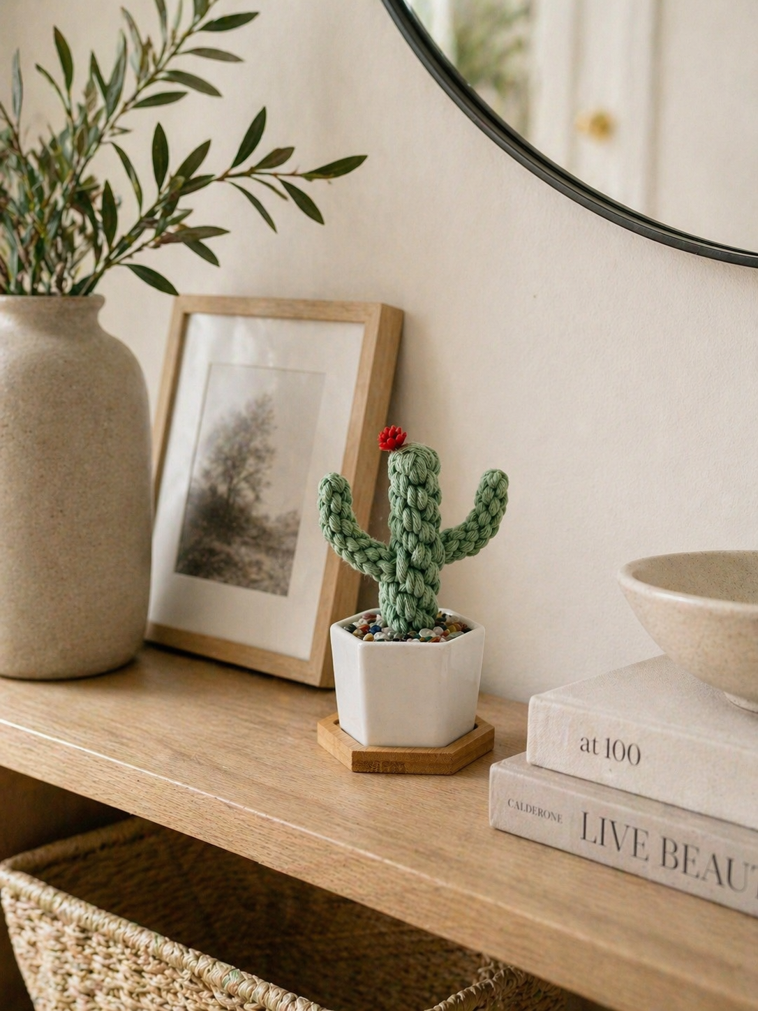 Handmade macrame cactus in white ceramic pot with crystal chips on bamboo tray styled on wooden shelf with mirror and olive branch vase, boho home decor