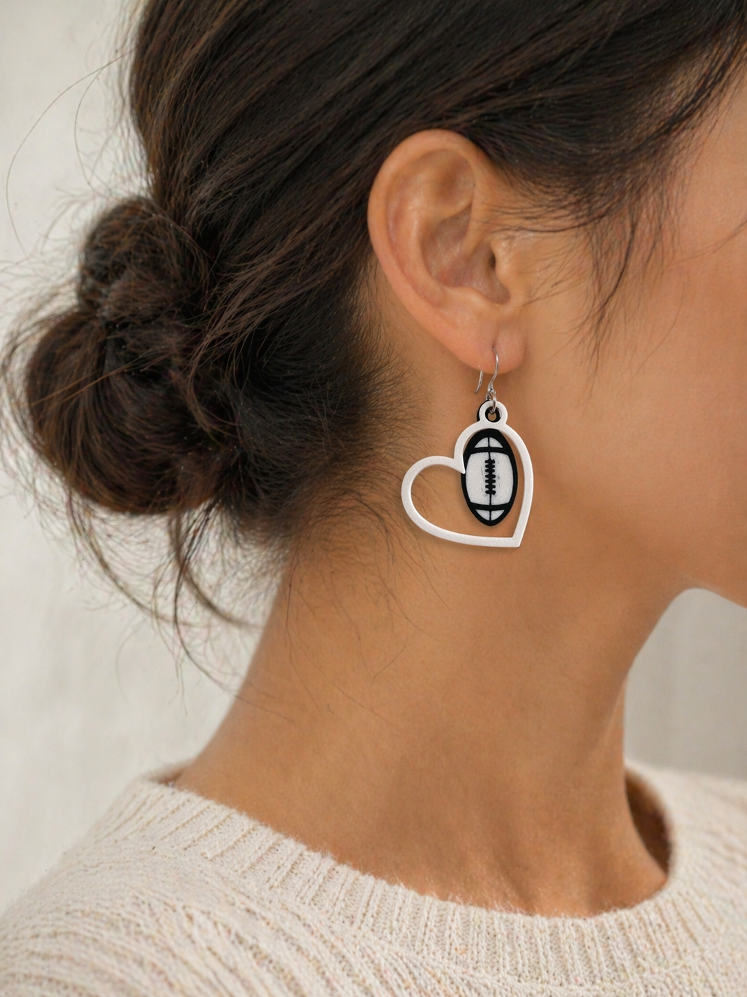 Heart-shaped earring with a football design worn by a person.