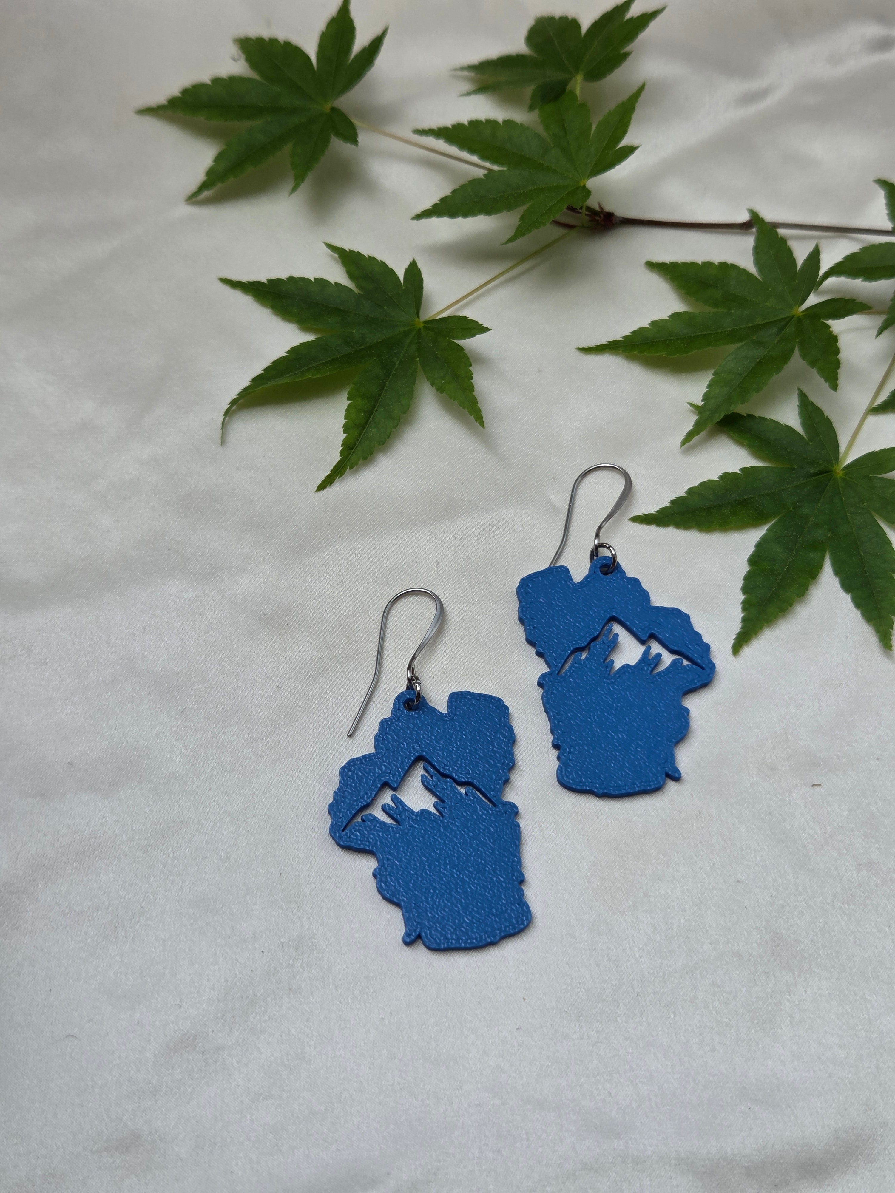 Blue sculpted Lake Tahoe shaped earrings with mountain cutout, silver French hook wires, displayed on white fabric with Japanese maple leaves