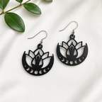 Black lotus flower earrings on a white background with green leaves.