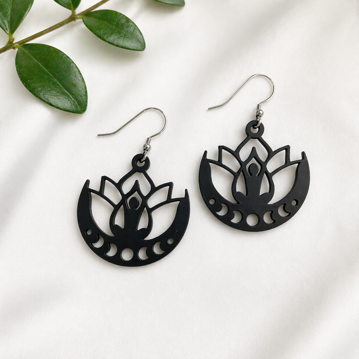Black lotus flower earrings on a white background with green leaves.