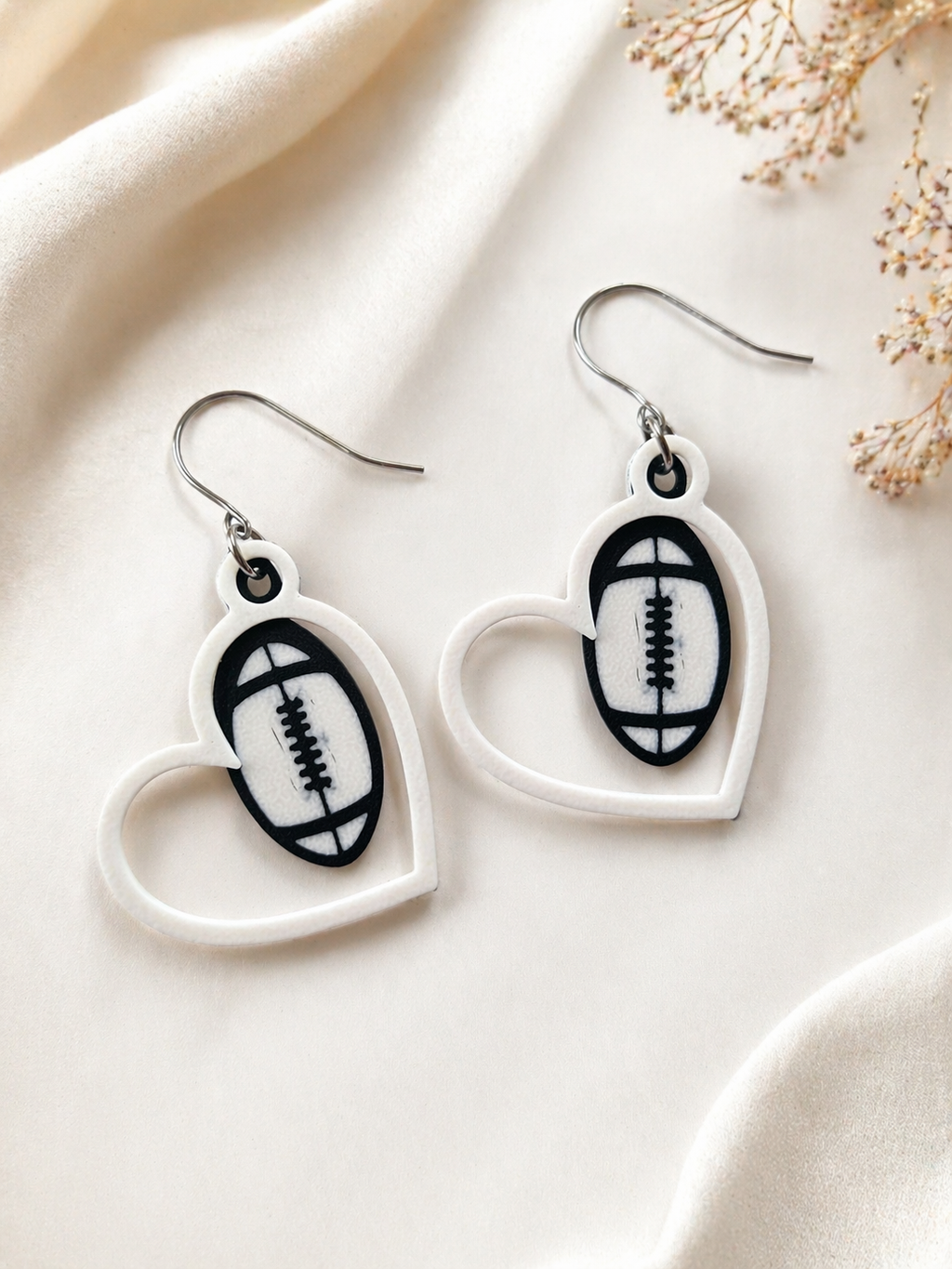 Heart-shaped earrings with football design on a light fabric background