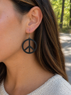 Woman wearing white sculpted peace circle dangle earring outdoors, lifestyle photo, silver French hook, retro boho jewelry