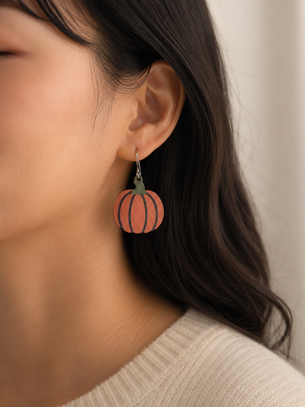 Close-up of a person wearing pumpkin-shaped earrings with a neutral background