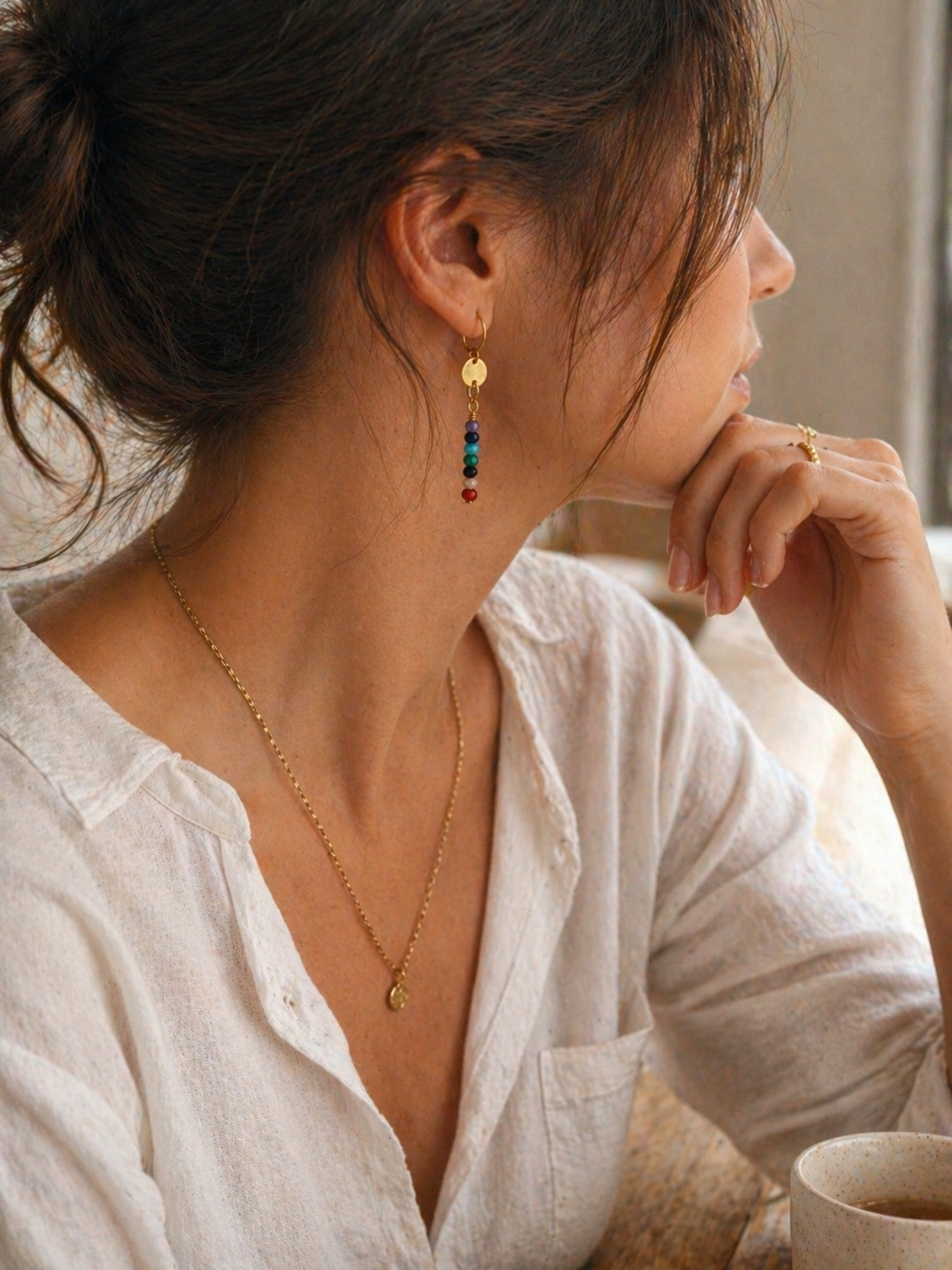 Woman wearing gold earrings and a necklace, sitting indoors.