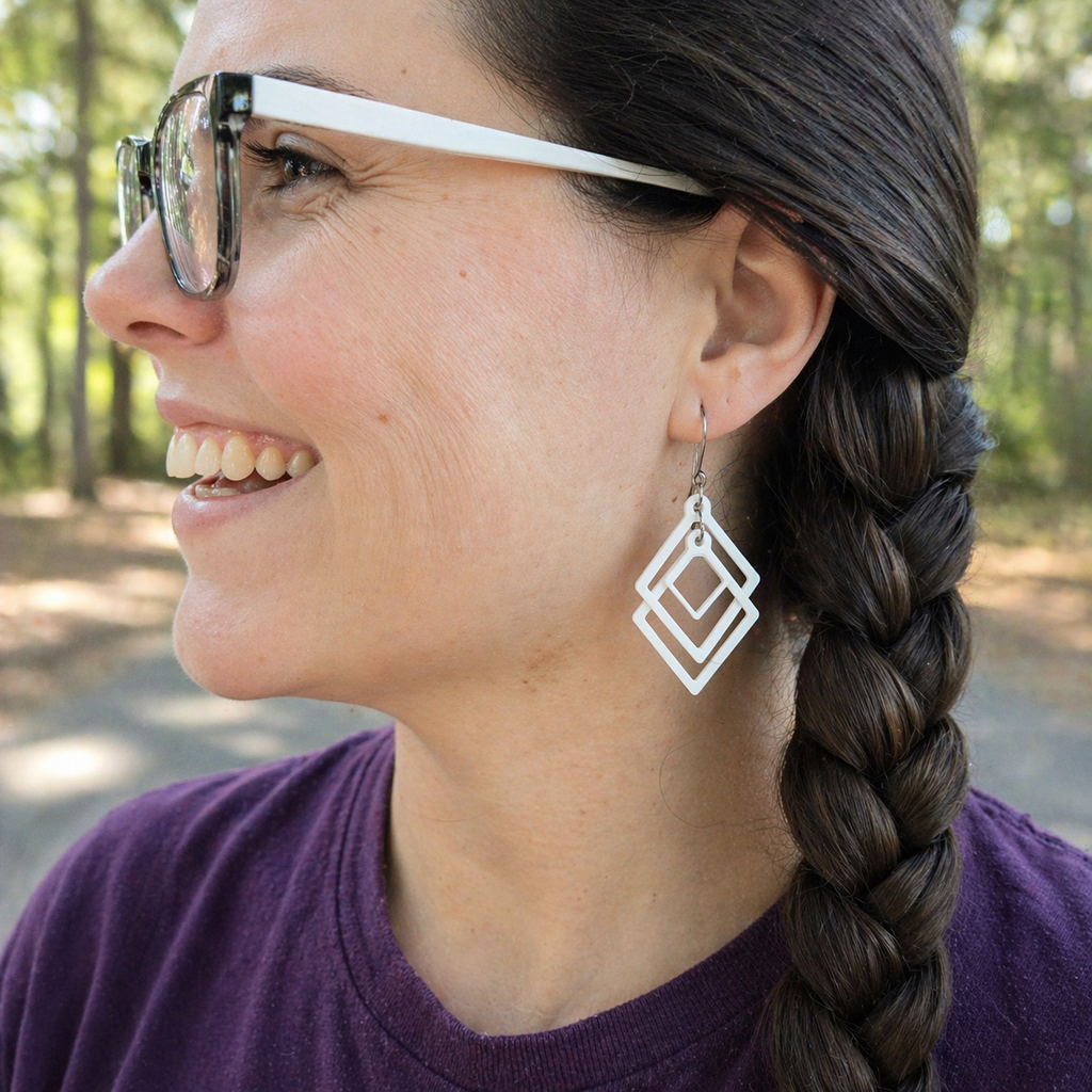Smiling woman wearing white sculpted open frame geometric earrings with silver French hook, minimalist diamond dangle jewelry