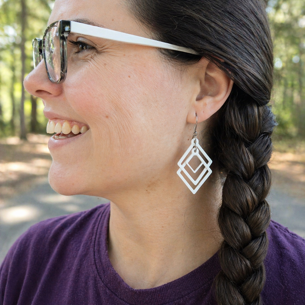 Smiling woman wearing white sculpted open frame geometric earrings with silver French hook, minimalist diamond dangle jewelry