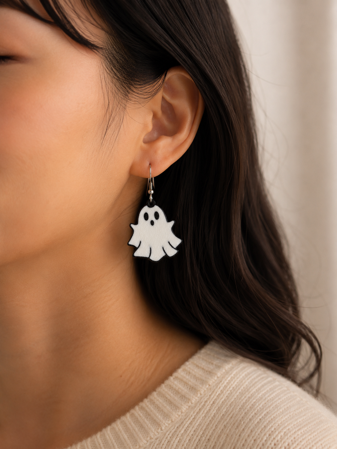 Close-up of a person wearing ghost-shaped earrings with a neutral background