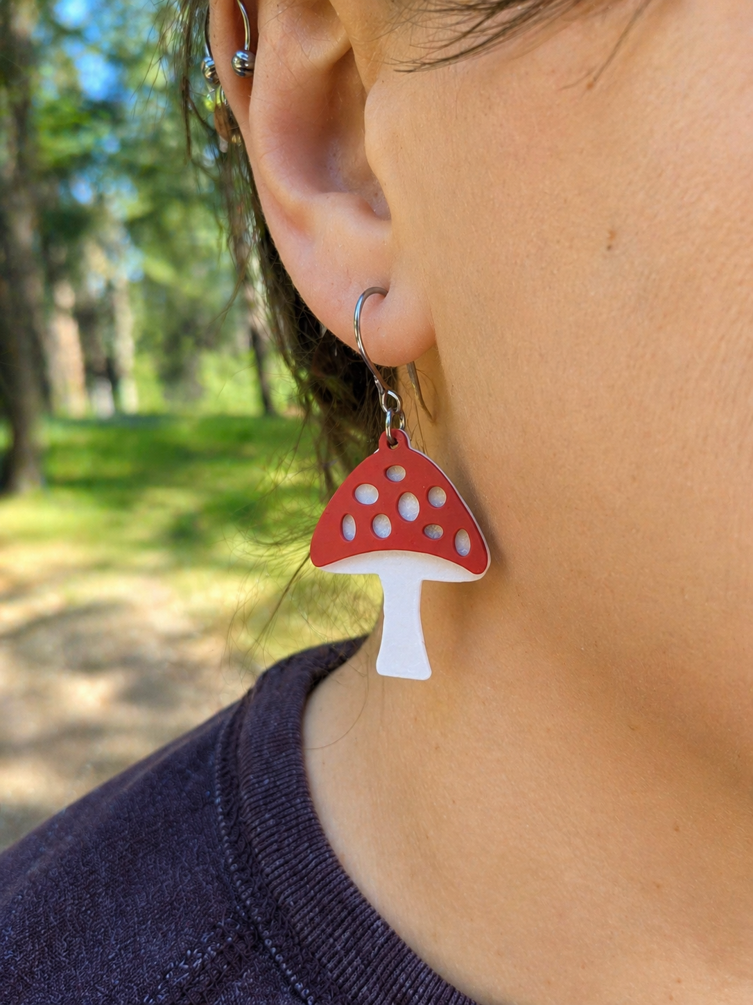 Mushroom-shaped earrings worn by a person with a blurred natural background