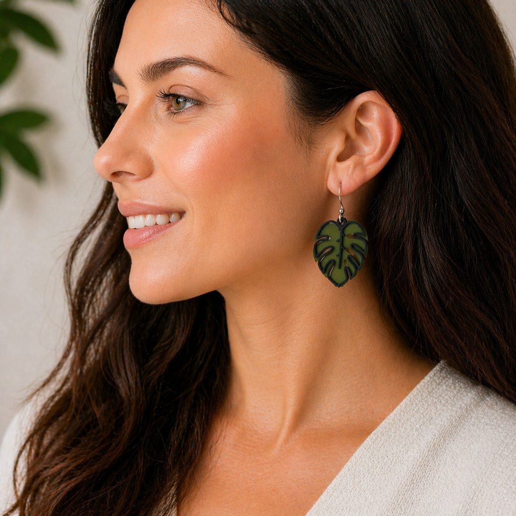 Woman smiling wearing green and black sculpted monstera leaf dangle earrings, tropical plant jewelry, silver French hook