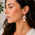 Woman wearing white sculpted cross earrings with cross cutout detail and wood tone accent, silver French hook, faith jewelry