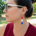 Woman wearing red white and blue sculpted star trio dangle earrings outdoors, patriotic cascading star jewelry with silver French hook